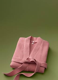 A folded pink waffle-knit robe with a matching belt displayed against a green background.