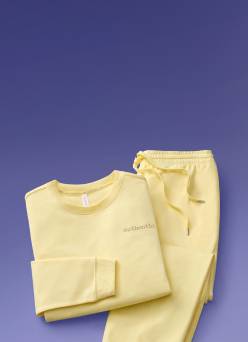 A yellow loungewear set with the word authentic written across the sweatshirt is displayed against a purple backdrop.