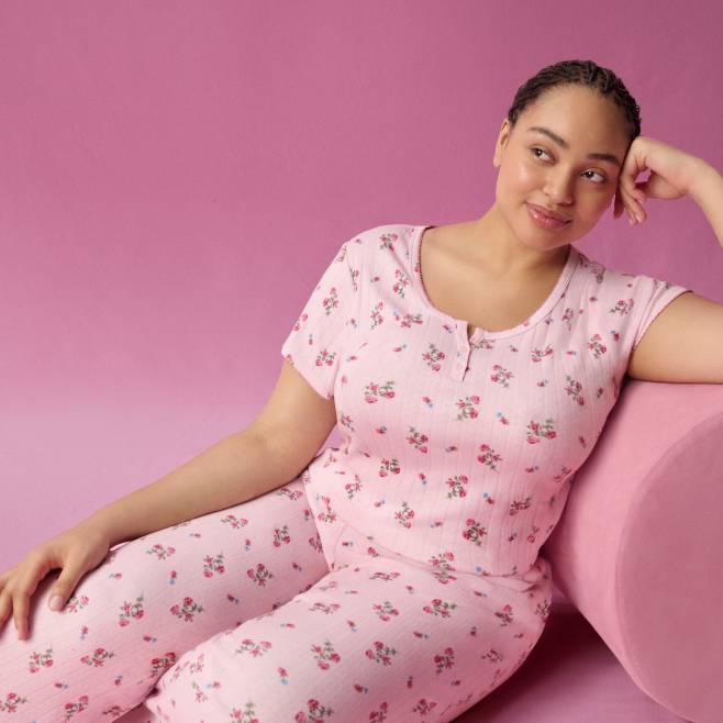 Woman in a pink floral pajama top with matching pajama pants reclines against a soft pink backdrop.