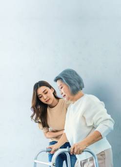 A woman helping an older woman using a walker is shown.