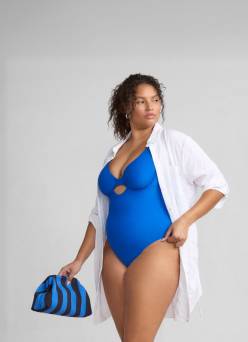 A woman is shown against a white, grey background wearing a white button-up long-sleeve swim cover-up shirt.