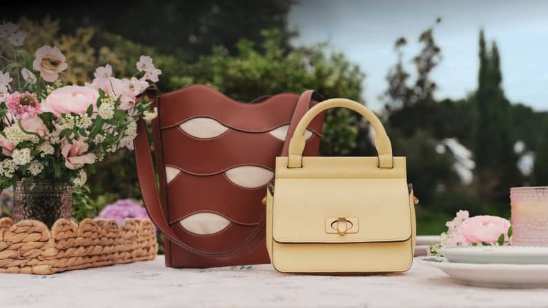 Cognag cutout bucket bag and yellow faux leather top handle mini bag on a table surrounded by garden party table decor.